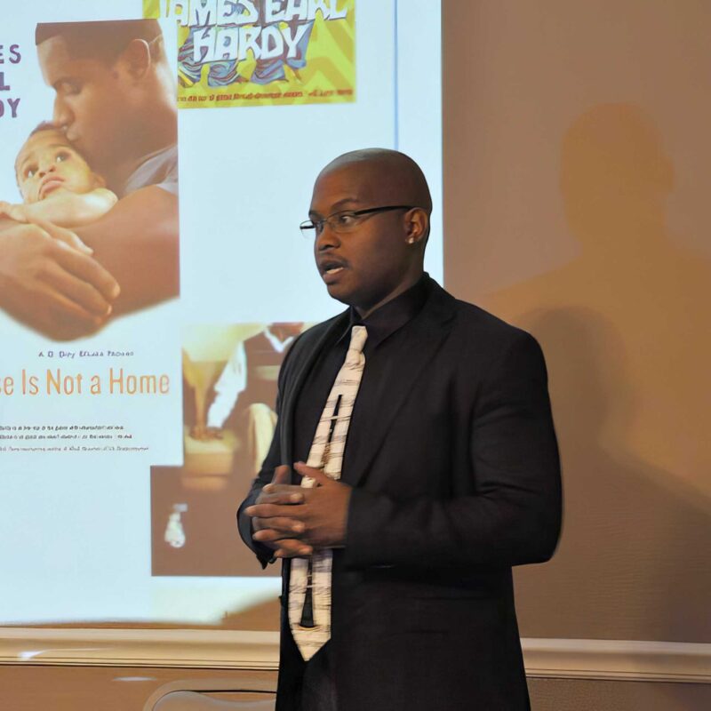 K. Murry Johnson stands at the front of a room delivering a lecture, with a projected presentation visible behind him.
