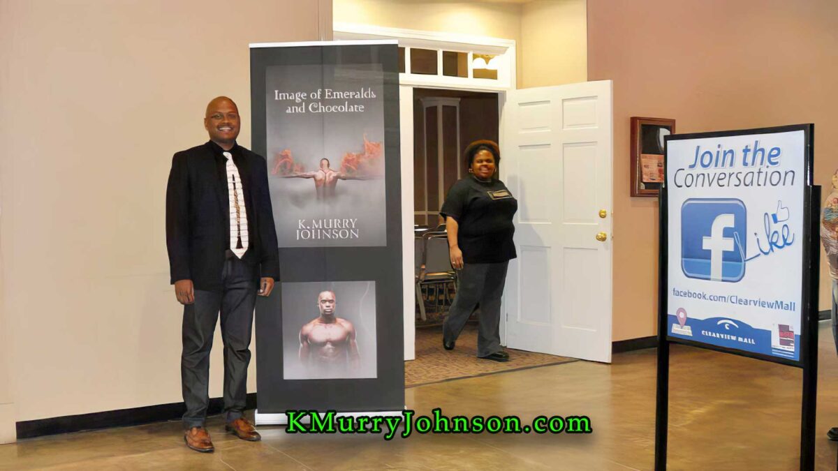K. Murry Johnson stands beside a promotional display for Image of Emeralds and Chocolate at a public event, with signage inviting attendees to join the conversation on social media.