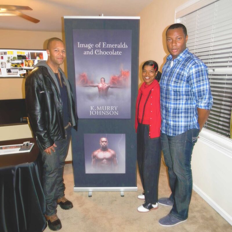 Three readers stand beside a promotional display for Image of Emeralds and Chocolate by K. Murry Johnson during a book signing event held indoors.
